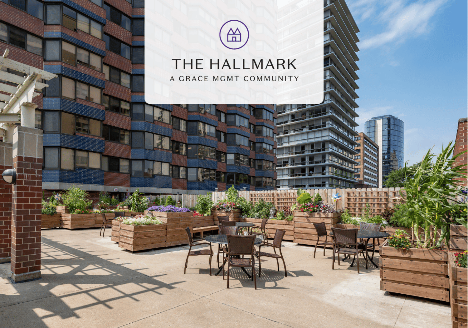 Rooftop courtyard with wooden planters and metal tables in an urban apartment complex; logo reads The Hallmark.